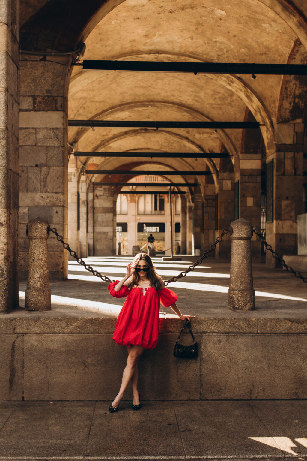 Woman in a red dress poses between the columns of the Palazzo della Ragione arcade on Piazza dei Mercanti in Milan.