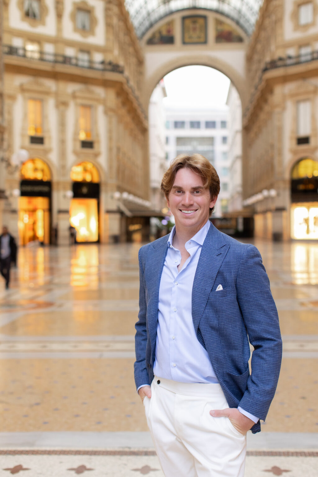 A smiling man in a blue houndstooth jacket standing under the arch of the Galleria Vittorio Emanuele II in Milan.