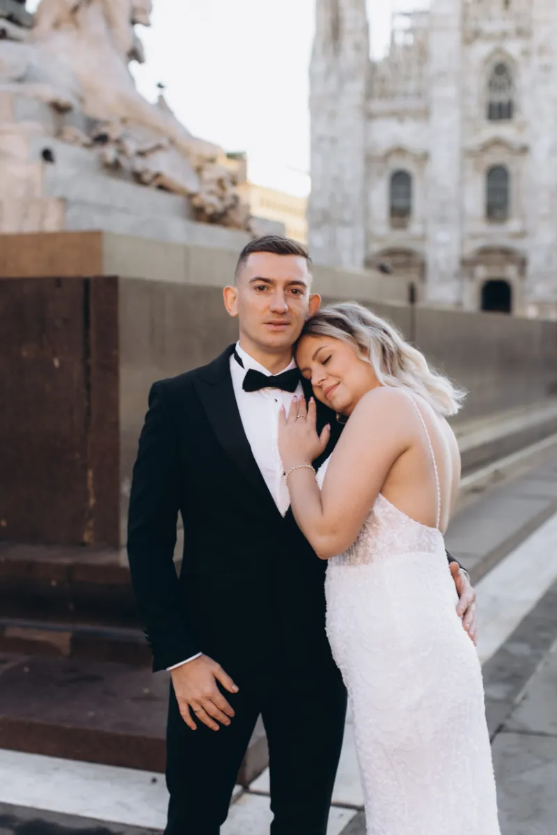 Engaged couple in a tuxedo and white dress embracing in Piazza del Duomo, Milan
