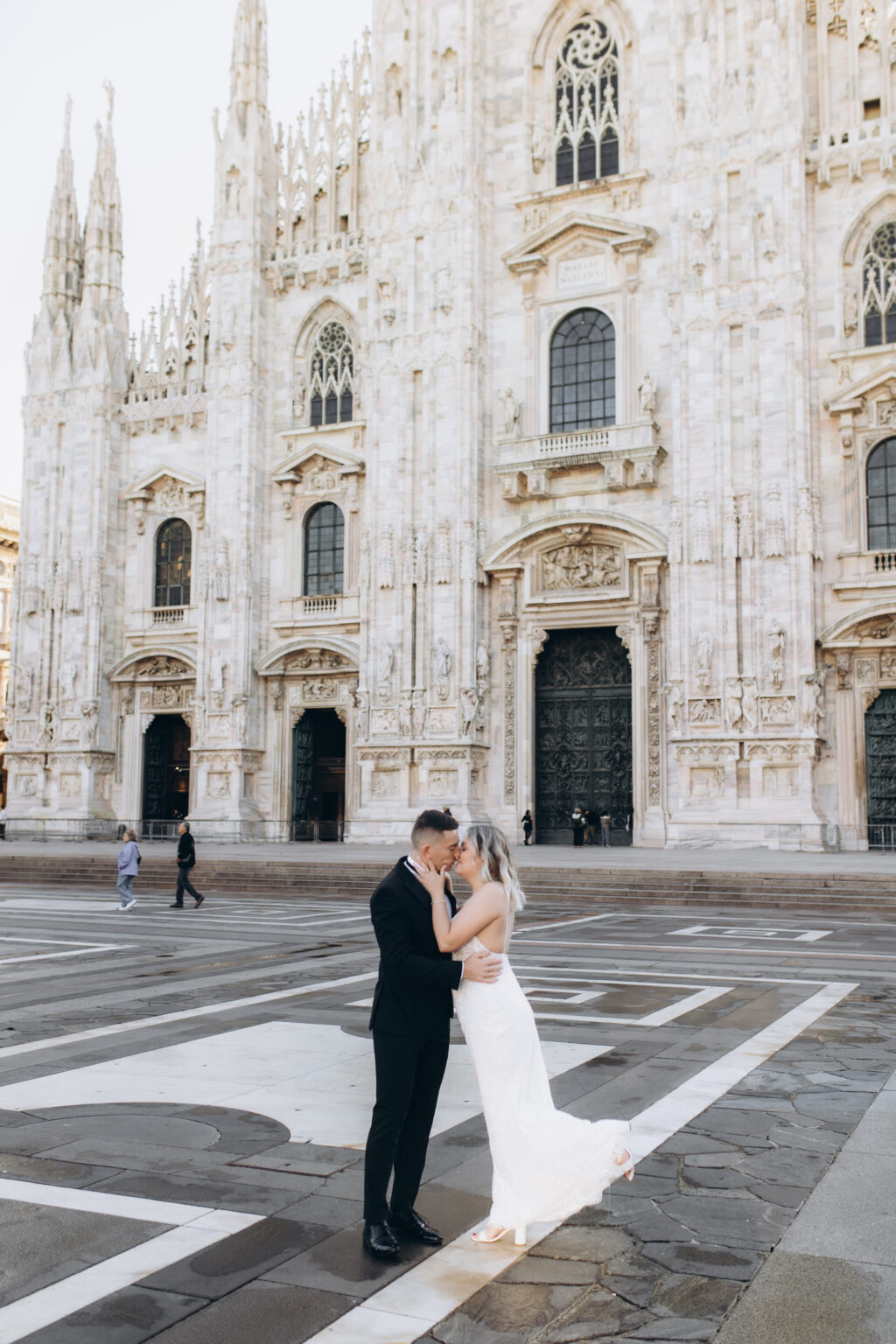 The couple share a kiss on Piazza del Duomo, the full Gothic marble facade of the Milan Cathedral rising behind them.