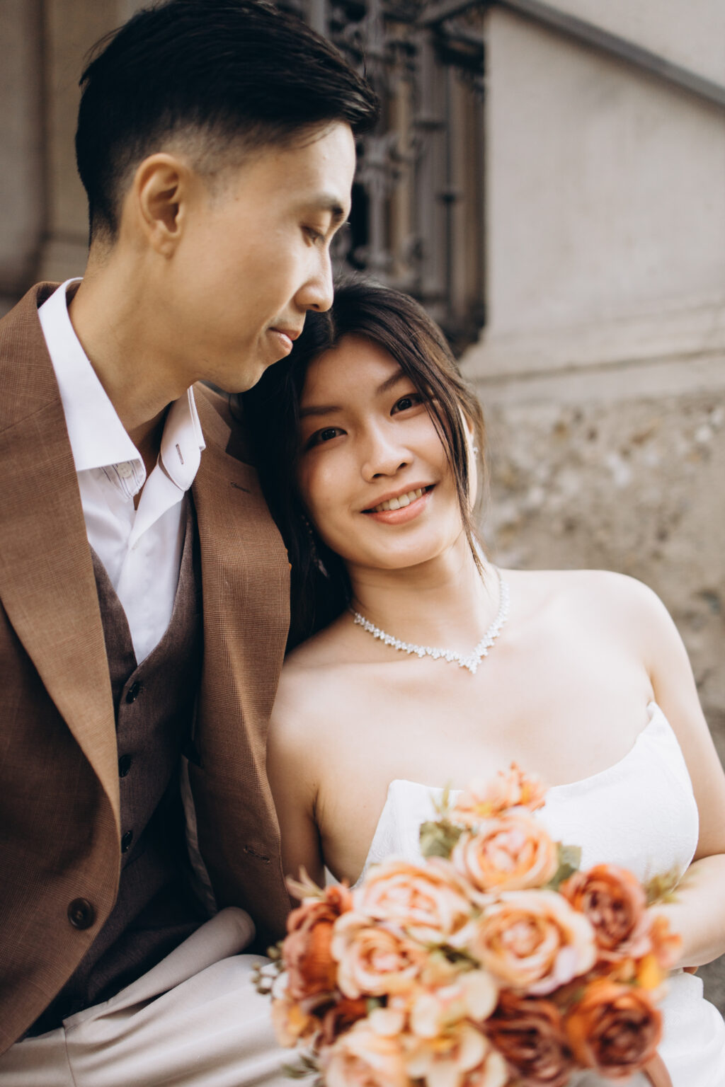 Groom-to-be resting his head against his smiling bride-to-be holding a peach rose bouquet in a historic corner of Piazza dei Mercanti in Milan