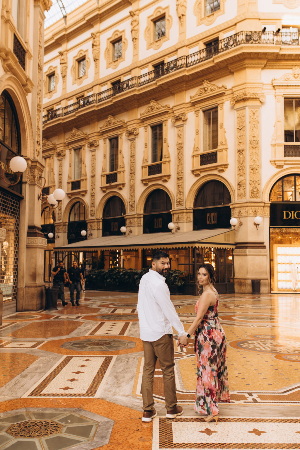 Parents of the quinceañera hold hands and glance back while walking across the mosaic floor of the Galleria Vittorio Emanuele II in Milan.