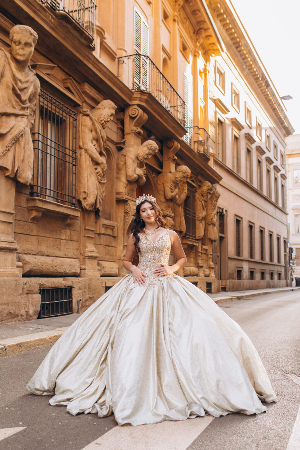 Quinceañera in a golden ball gown poses before the stone telamones of the Casa degli Omenoni on Via degli Omenoni during her quinceañera photoshoot in Milan.