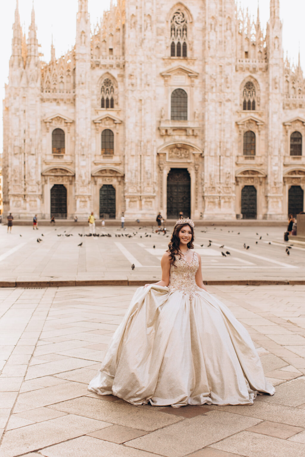 Quinceañera in a golden ball gown poses before the marble Gothic facade of the Duomo di Milano in Piazza del Duomo.
