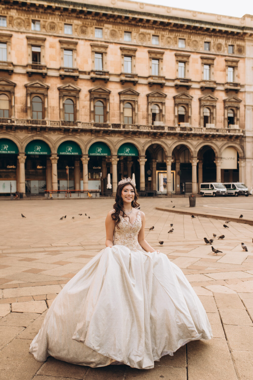 Quinceañera seated with her gown spread in Piazza del Duomo before the arcaded palazzo on the square's south side.