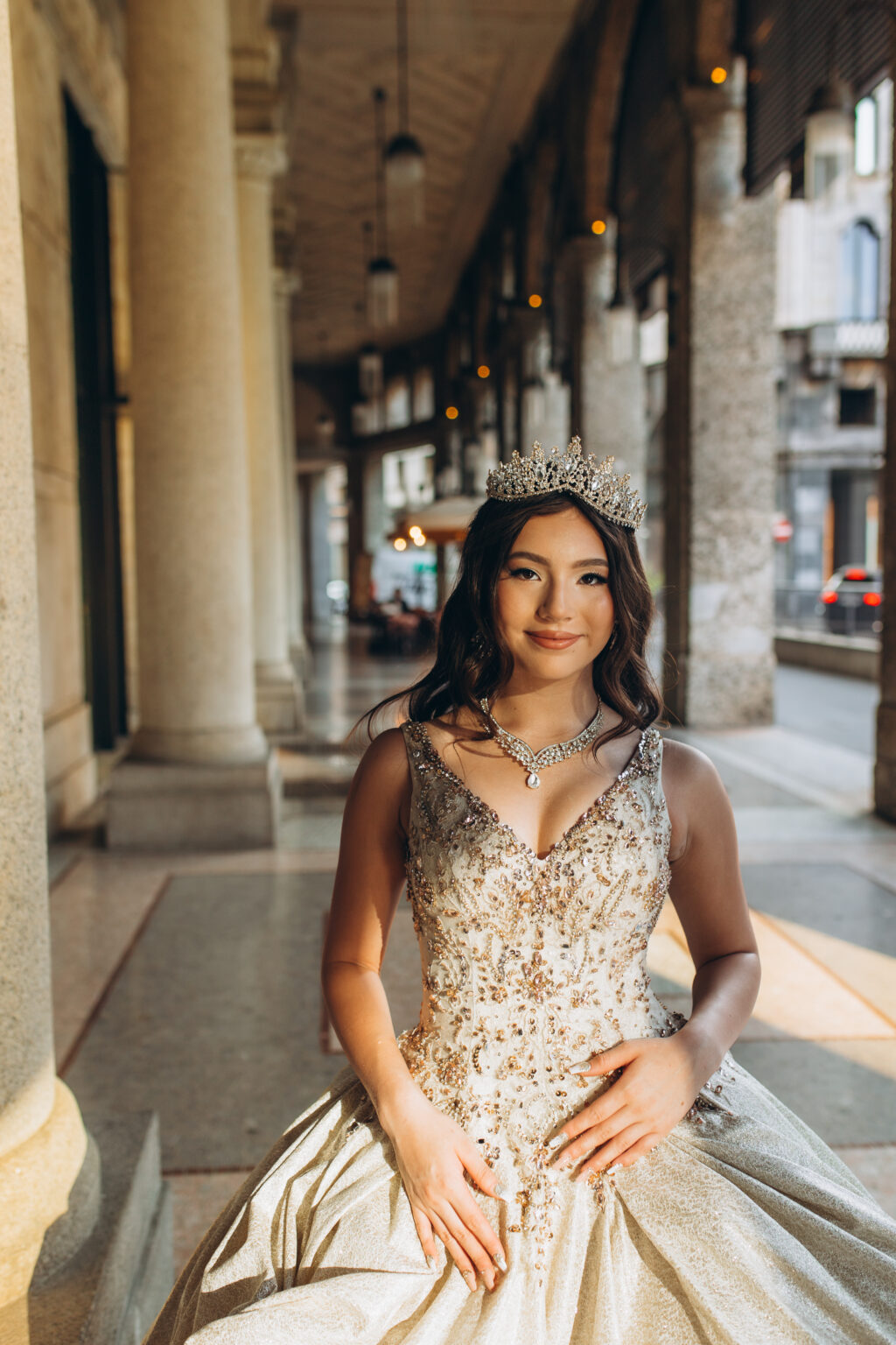 Quinceañera in a crown seated beneath the historic porticoes of central Milan, a serene quinceañera portrait in Milan.