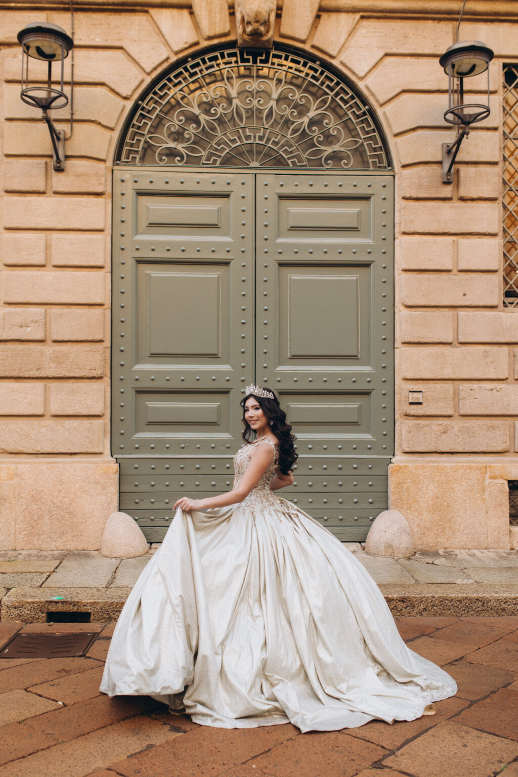 Quinceañera twirling her golden gown in front of a grand arched green palazzo door in central Milan.