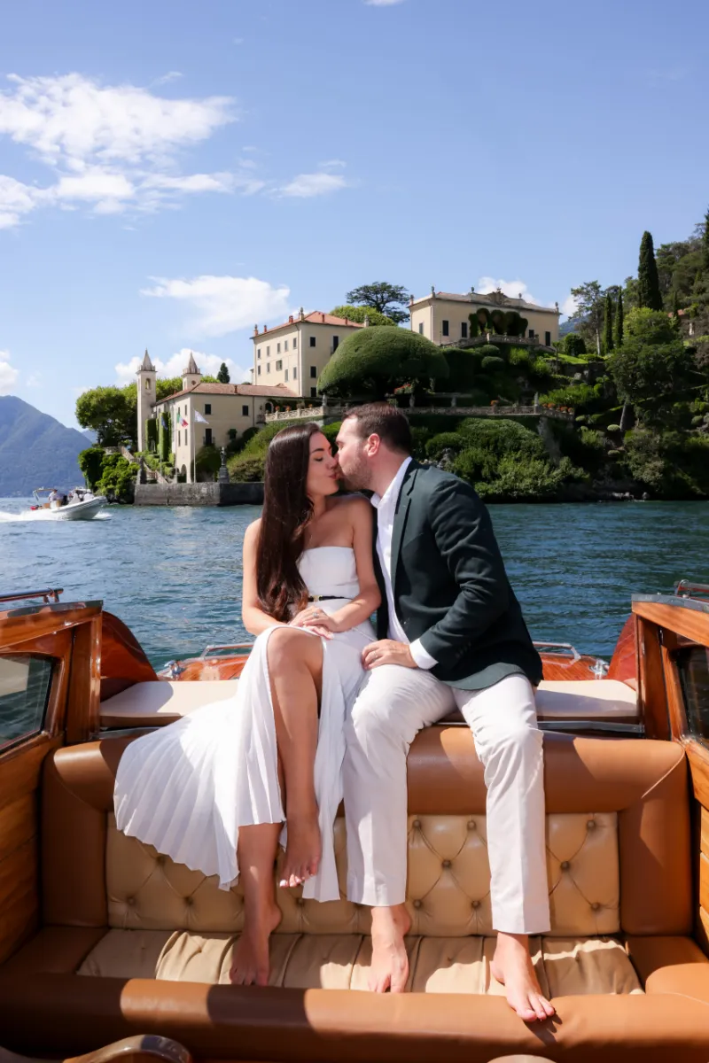 Couple kissing on a wooden boat in front of Villa del Balbianello, Lake Como