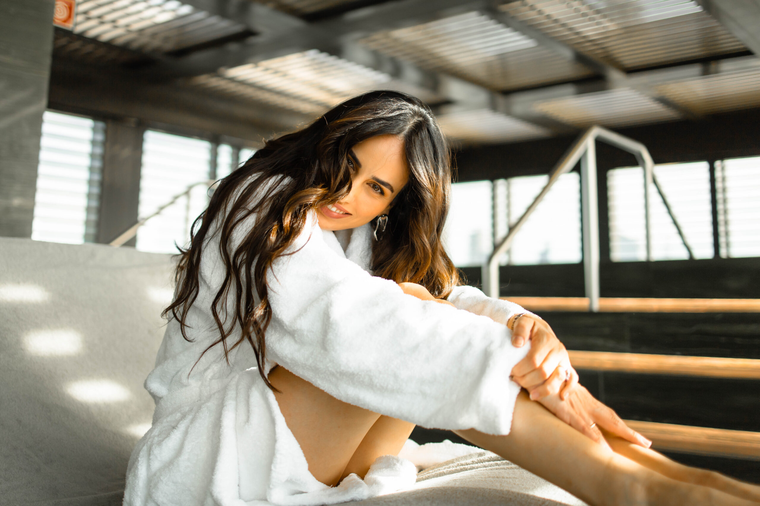 Warm Indoor Light Portrait in Milan A woman in a white robe sits in warm sunlight streaming through louvered blinds at an indoor spa in Milan