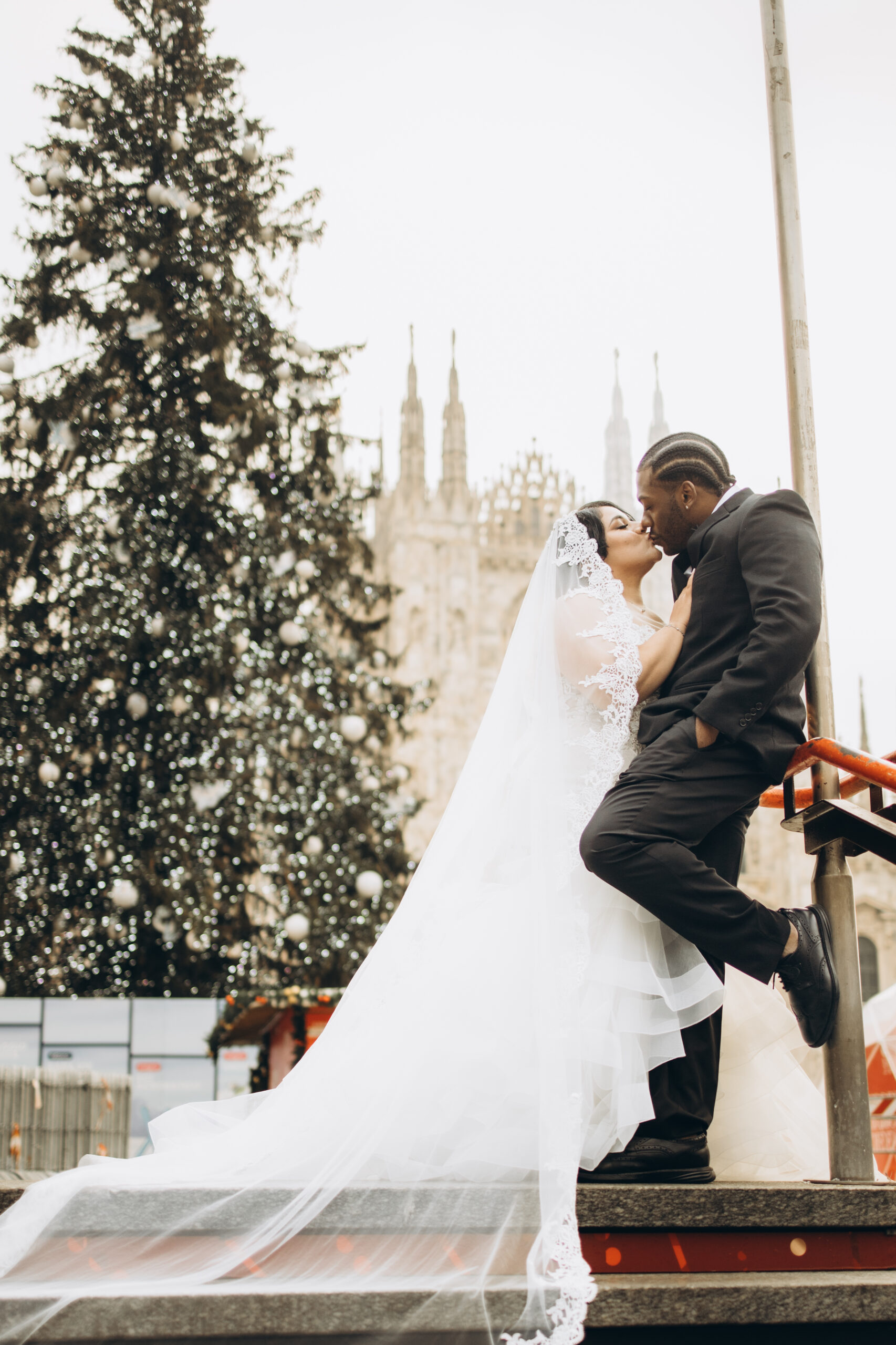 Winter Wedding Photoshoot by the Christmas Tree at the Duomo, Milan A bride and groom kiss beside the giant Christmas tree in front of the Duomo cathedral in winter in Milan