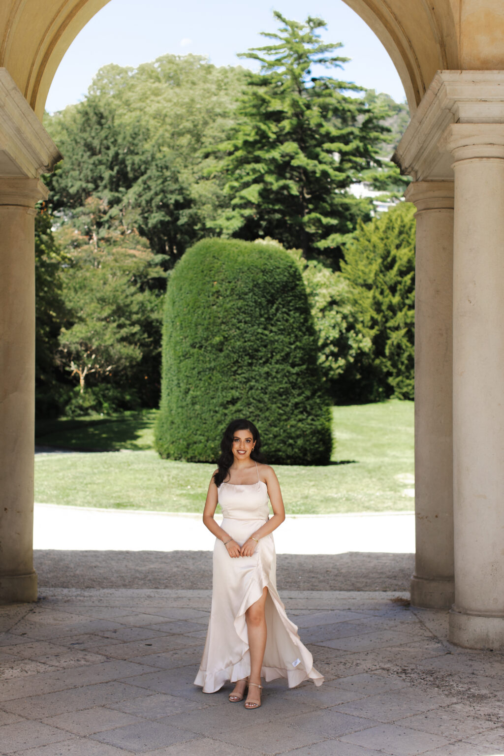 Woman in a champagne dress standing beneath a grand arched villa colonnade framing a topiary garden on Lake Como