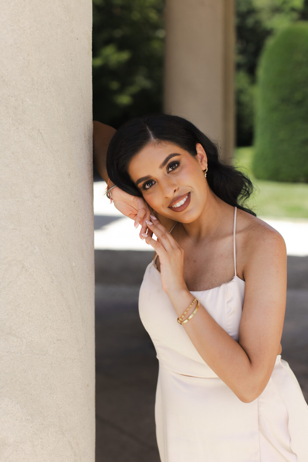 Smiling woman in a champagne dress leaning against a stone column of a villa colonnade on Lake Como