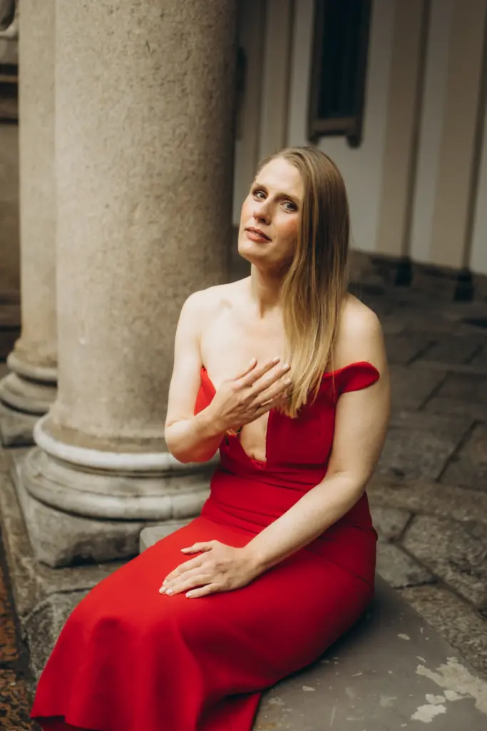 A woman in a red dress sitting by a stone column under the arcades of Brera, Milan