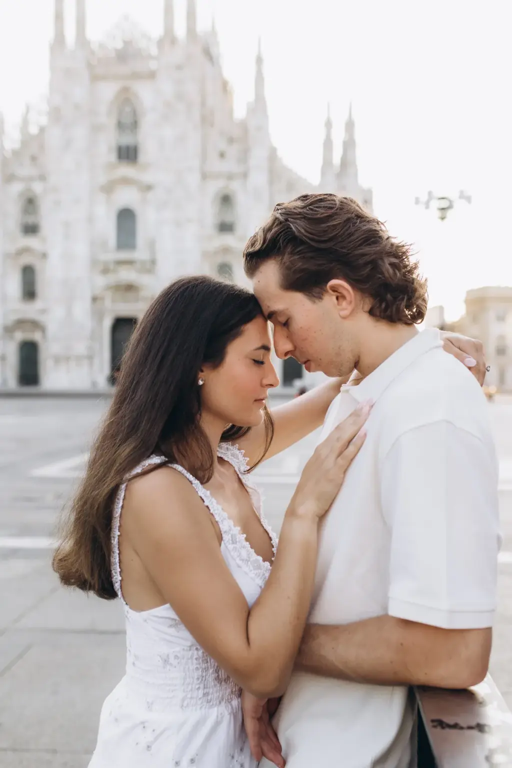 Eyes closed, a couple in white rest their foreheads together, her hand on his chest, with the Duomo facade rising behind them.