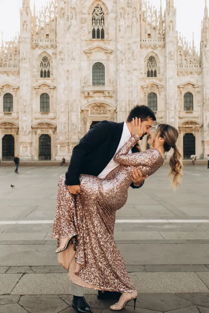 A man in a dark blazer dips a woman in a rose-gold sequin gown into a kiss in the middle of the square before the Duomo di Milano.