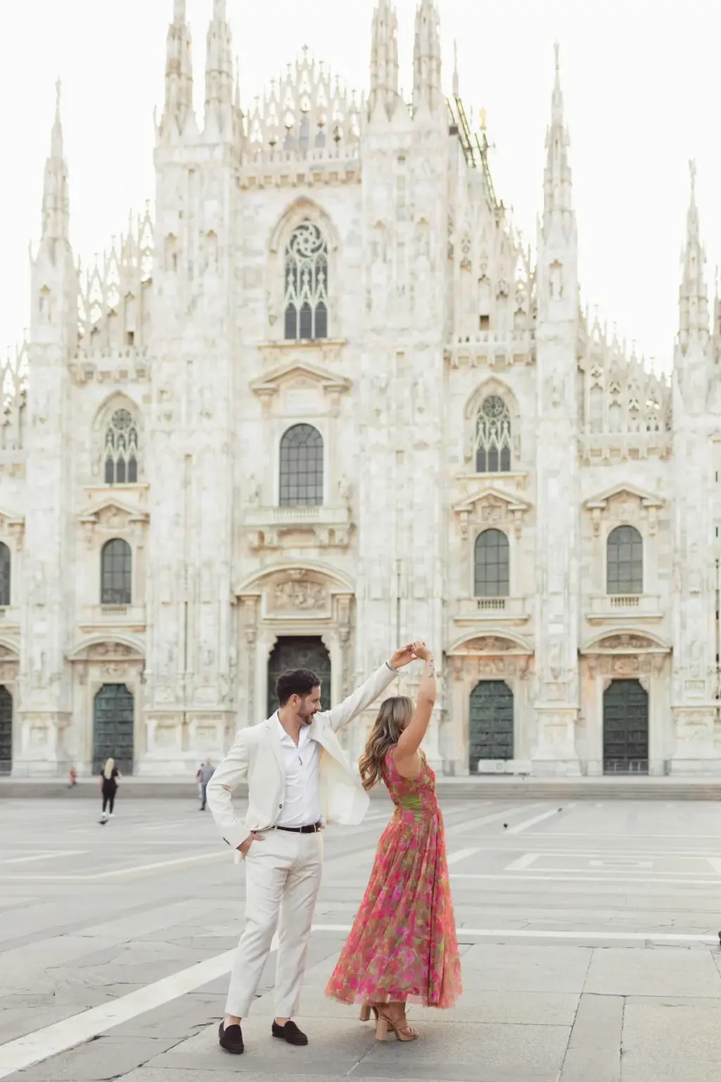 He lifts her hand high to spin her, her back to the camera, as the gothic facade of the Duomo di Milano fills the frame.