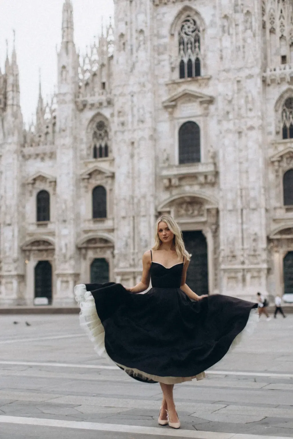 Standing alone before the Duomo di Milano, she fans out her full black skirt to show the white tulle petticoat beneath.