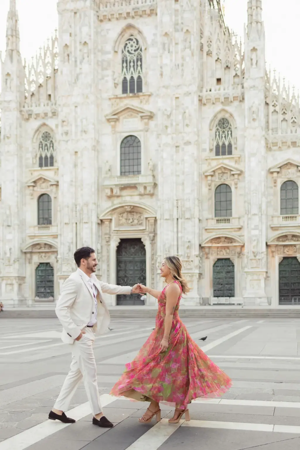 Holding hands at arm's length, the couple dances on the Duomo square as her pink floral dress swirls around her ankles.