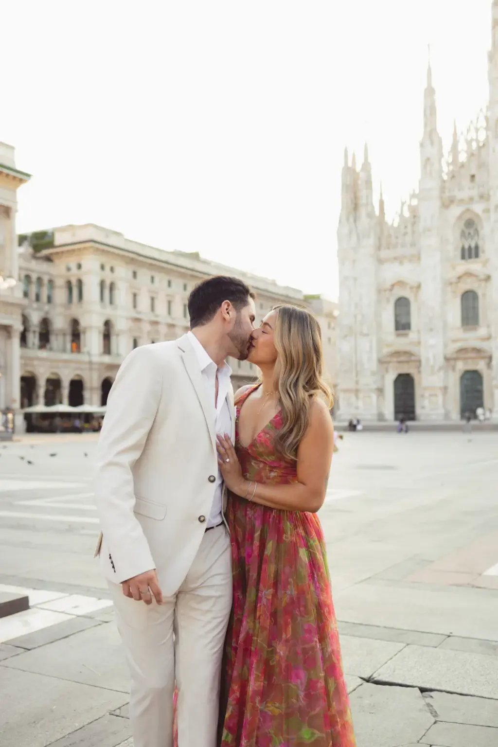 The couple kisses on the edge of the Duomo square, the cathedral spires to the right and pale palazzos lining the left side.