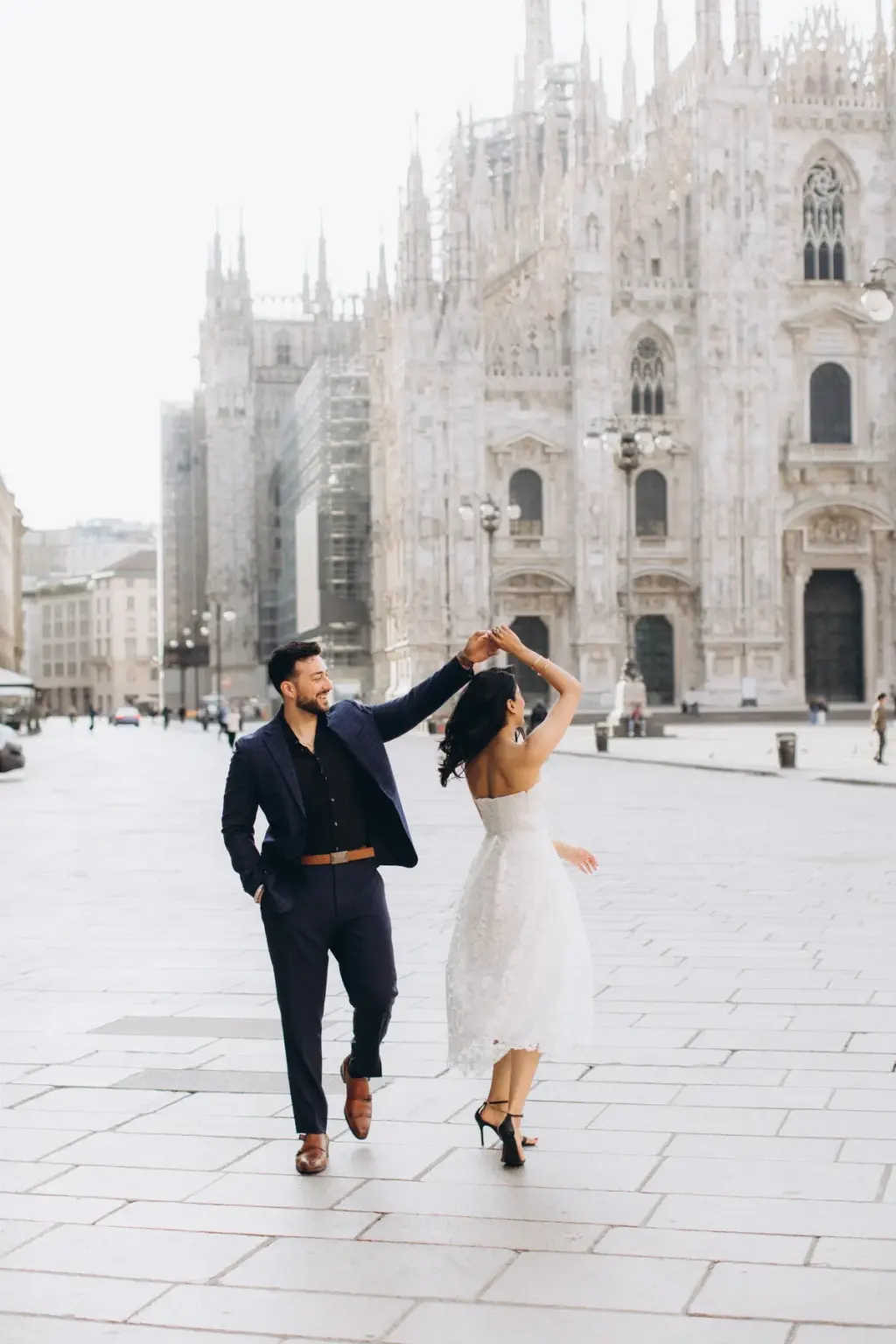 He raises her hand to spin her on the Duomo square, her white lace skirt swinging and black heels mid-step on the stones.