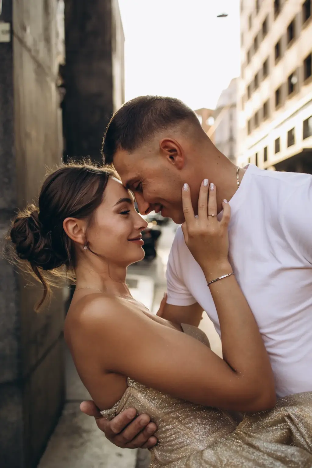 Smiling with closed eyes, a woman in a gold gown rests her forehead against her partner's as he holds her close on a Milan street.