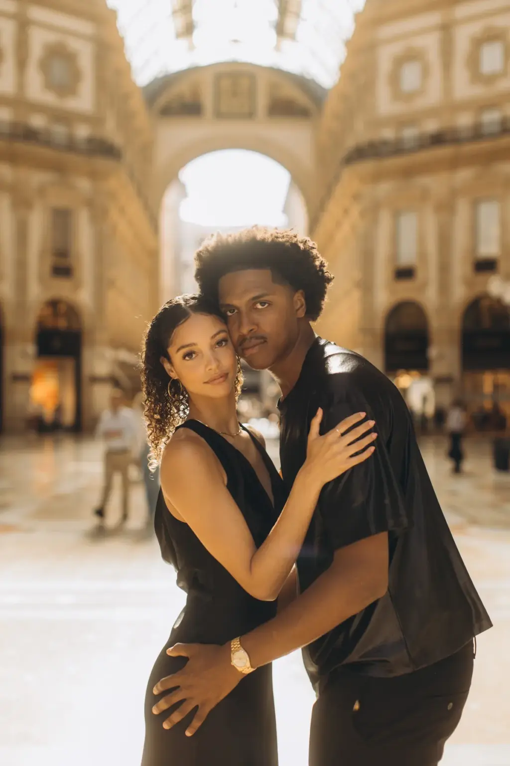Under the glass vault of the Galleria Vittorio Emanuele II, a couple in black stand close, her hand on his chest and his on her waist.