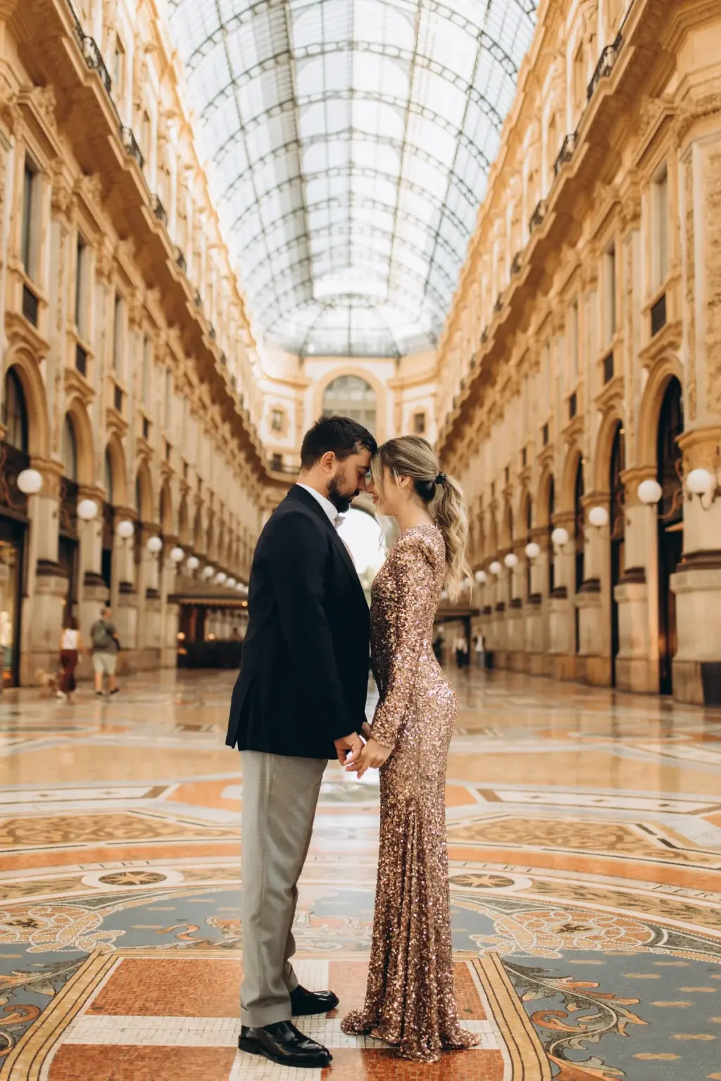 A couple stands forehead to forehead on the patterned marble floor of the Galleria, the long glass vault stretching behind them.