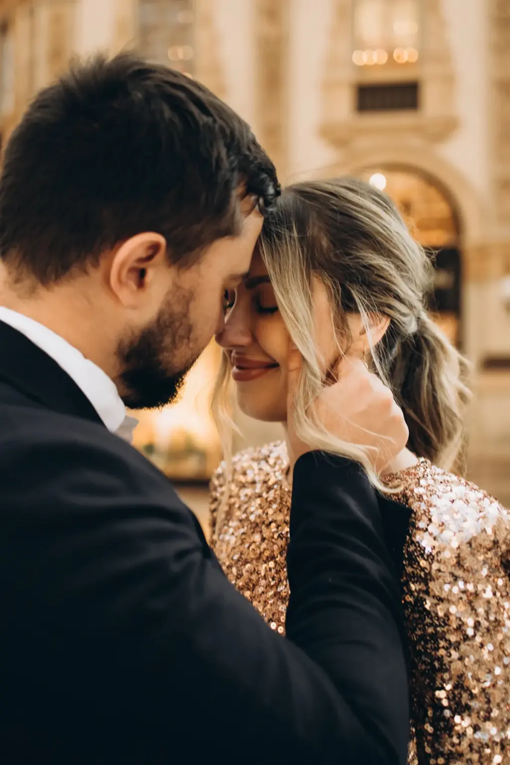 Close-up of a man gently tucking his partner's hair behind her ear as she smiles with eyes closed inside the Galleria.