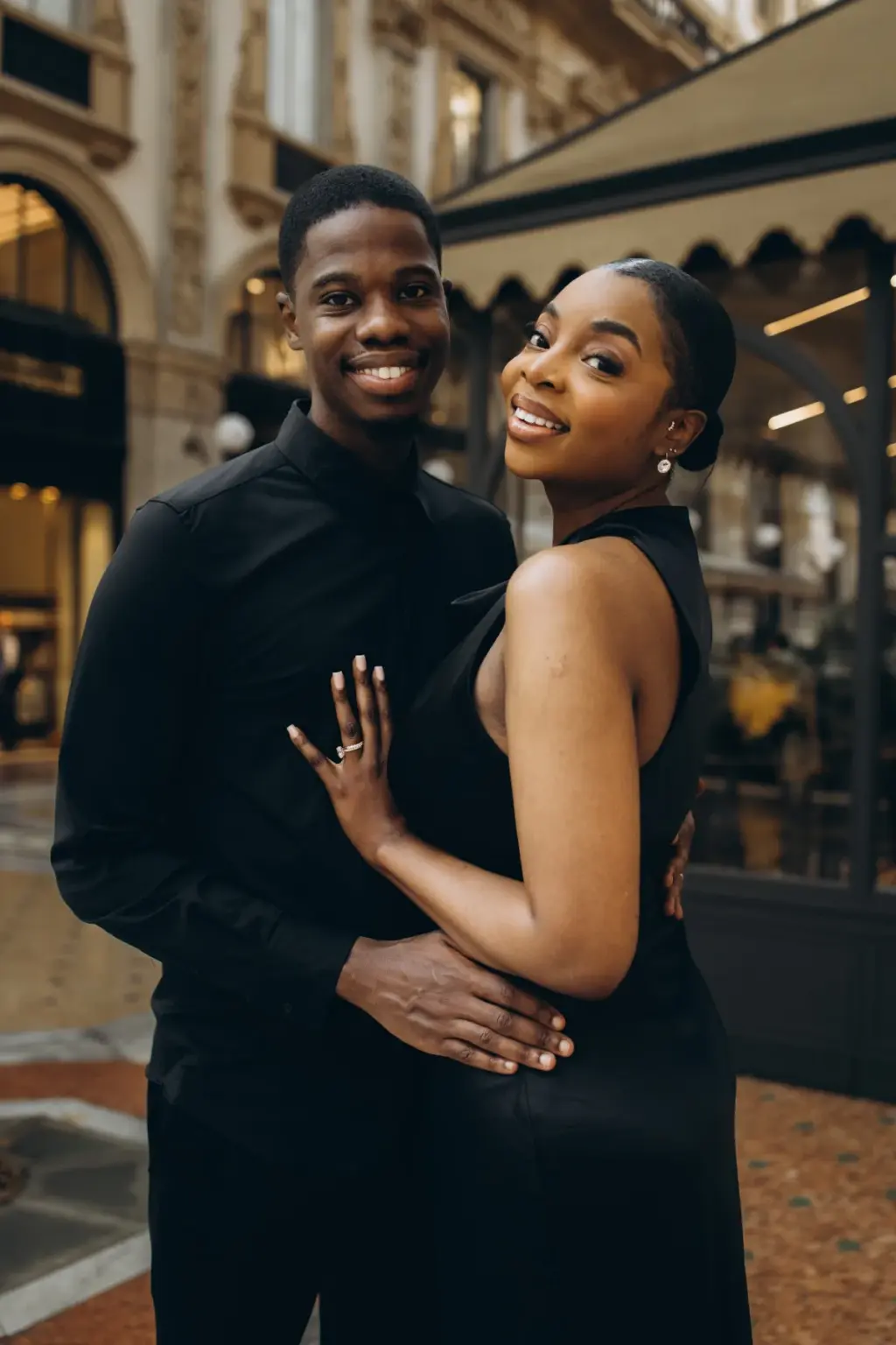 Both beaming at the camera beside a café awning in the Galleria, her ringed hand resting on his black shirt.