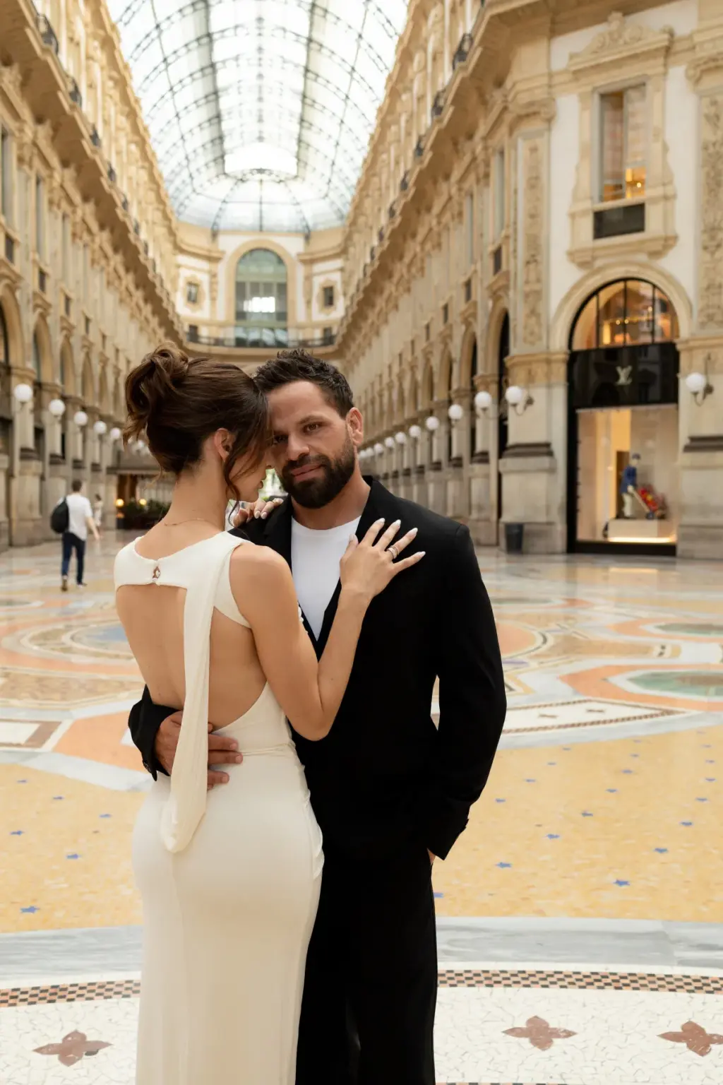 Her open-back dress faces the camera as she touches his chest and he smiles down at her on the Galleria's mosaic floor.
