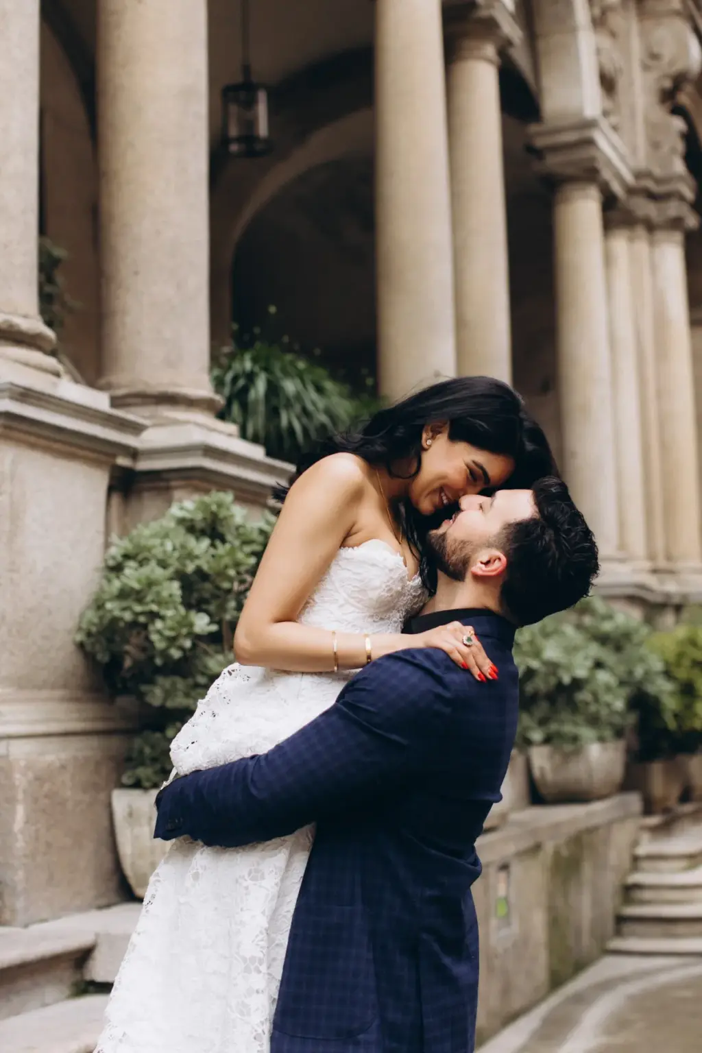 He lifts her high in a hug as she laughs down at him, among stone columns and potted shrubs in a Milan palazzo courtyard.