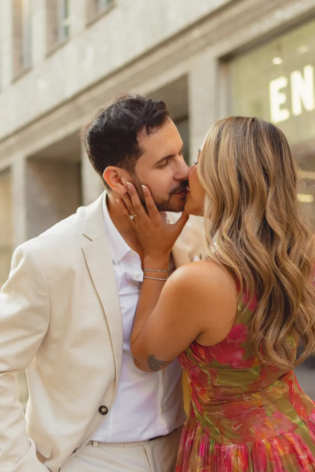 Close-up of a kiss on a Milan side street, her ringed hand on his cheek and his cream jacket against her floral dress.