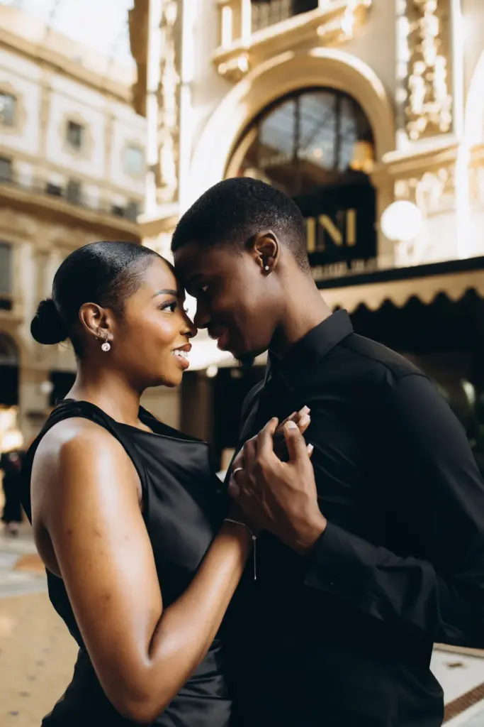 A couple dressed all in black rests forehead to forehead, hands clasped, in front of the Savini sign inside the Galleria.