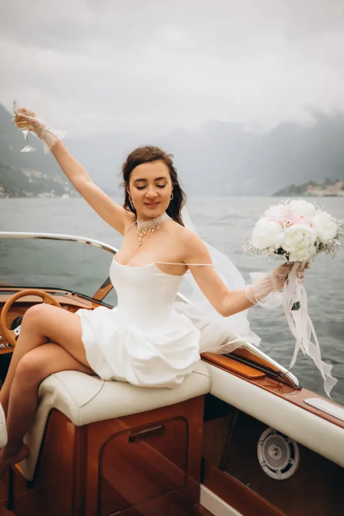 A bride raising a glass on the stern of a wooden boat on Lake Como