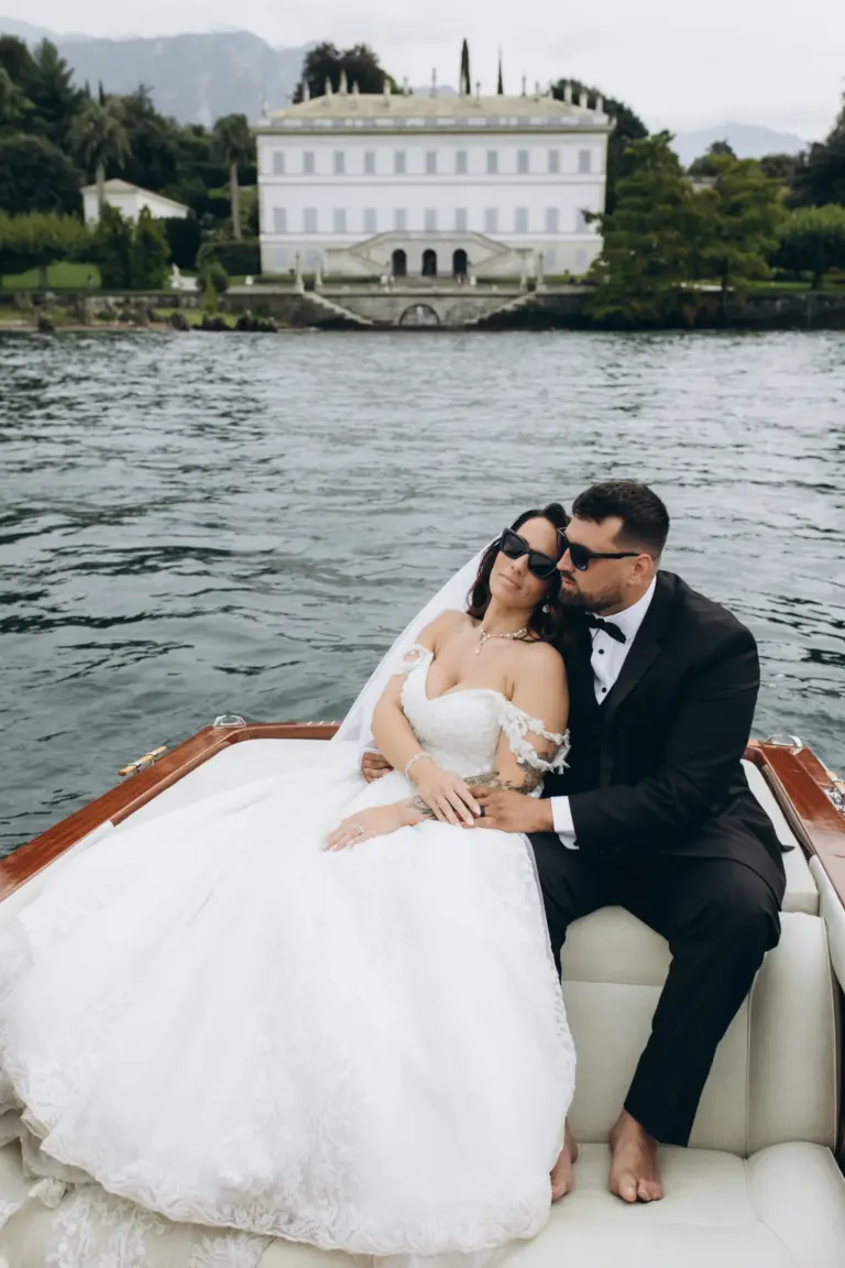 Bride and groom on a wooden boat in front of a lakeside villa on Lake Como