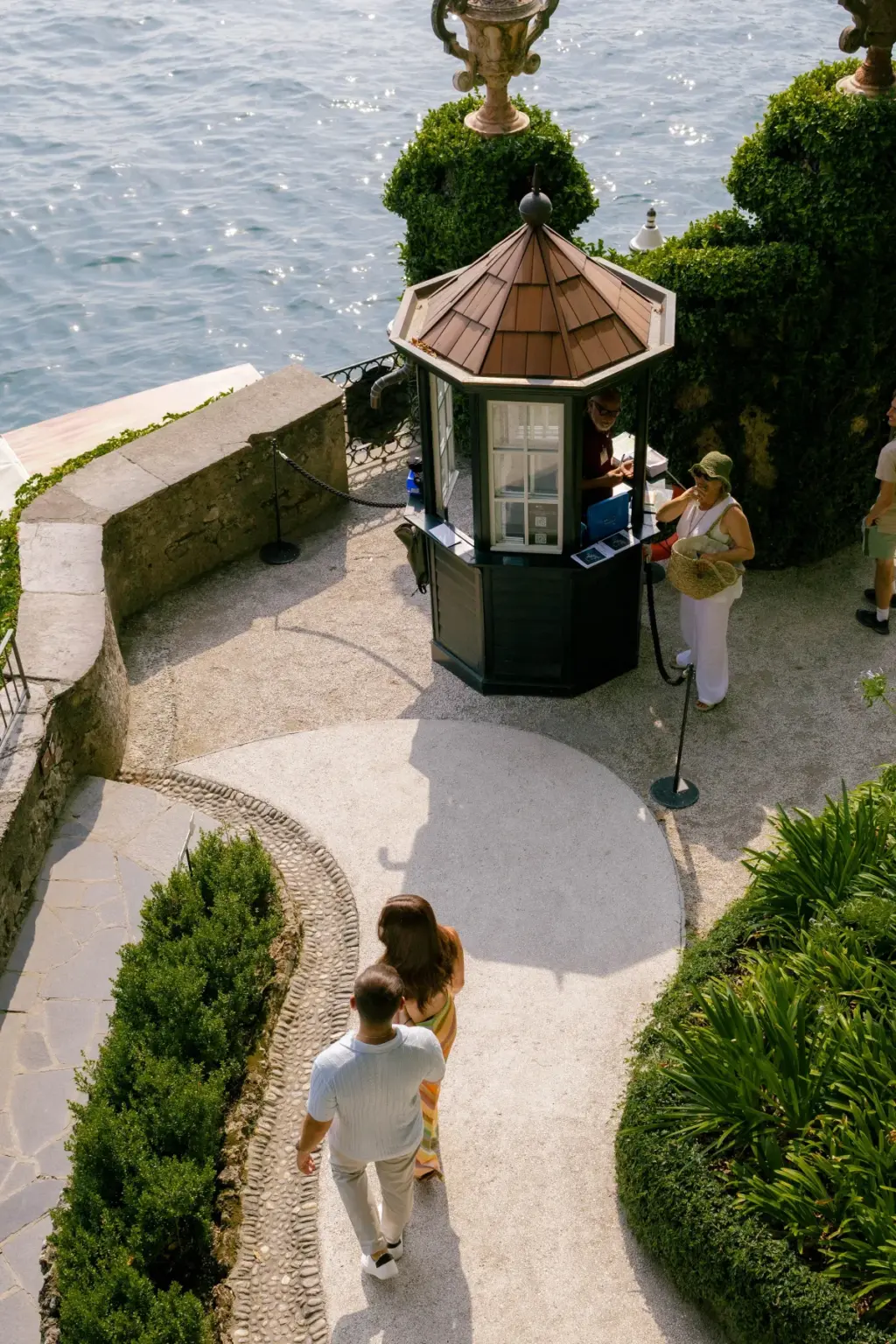 Looking down from above, a couple walks past the small octagonal kiosk on the lakeside terrace of Villa del Balbianello.