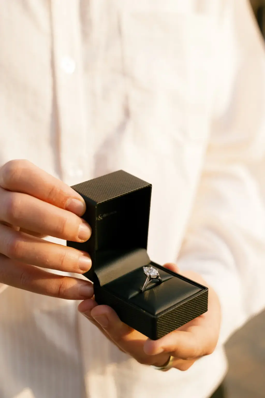 Close-up of a man's hands opening a black ring box with an engagement ring inside on Piazza del Duomo.