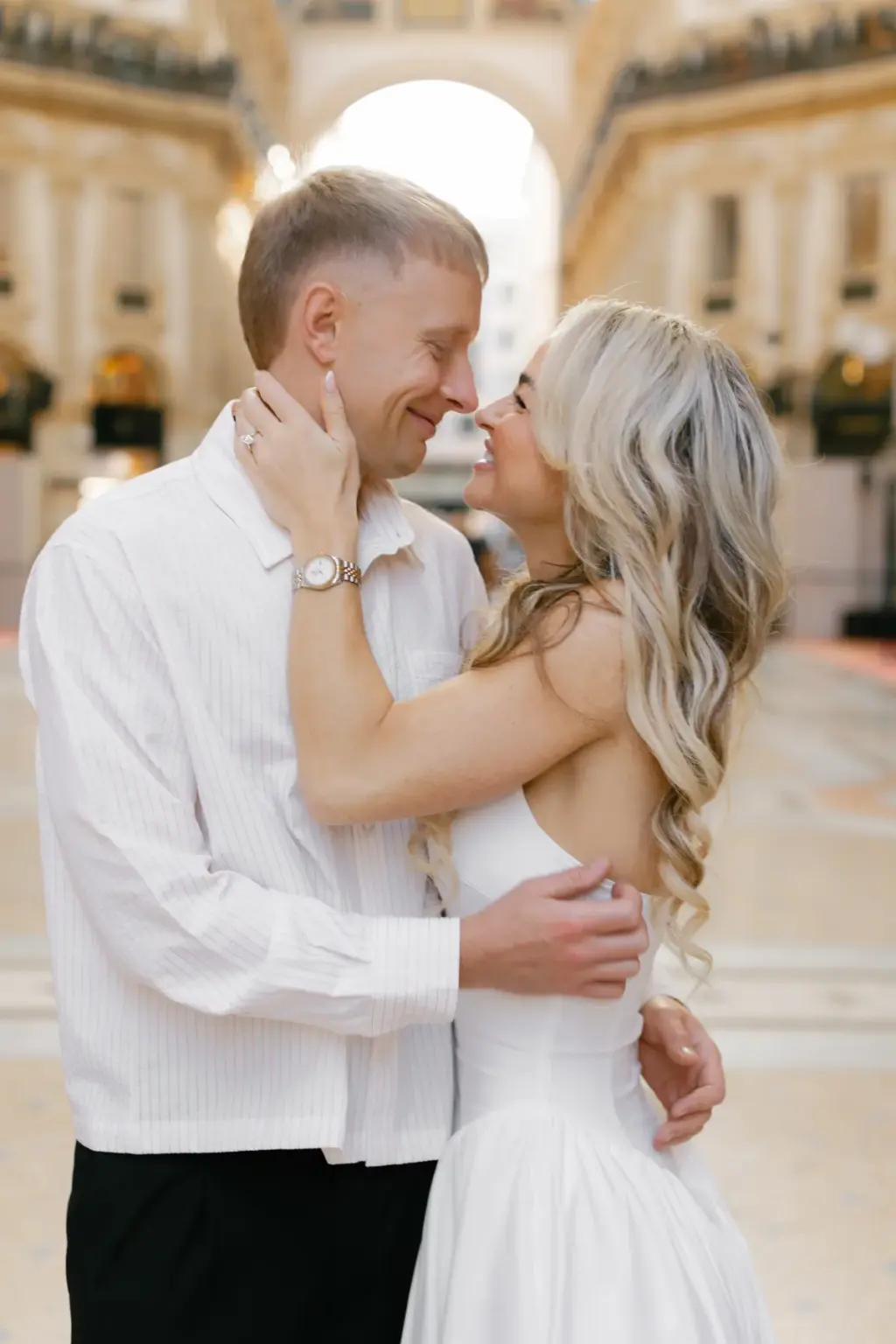 Nose to nose and smiling, a couple hold each other close in the Galleria, her hand resting on his cheek under the glass arch.