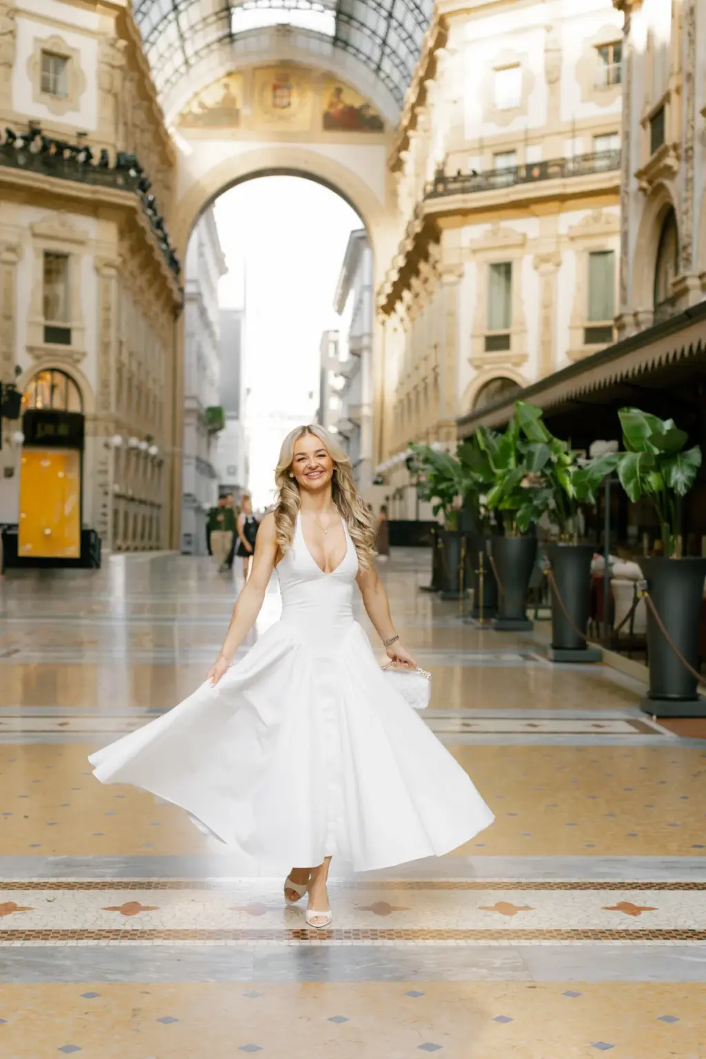 A woman in a full white skirt swirls the fabric as she walks along the mosaic floor of the Galleria Vittorio Emanuele II.